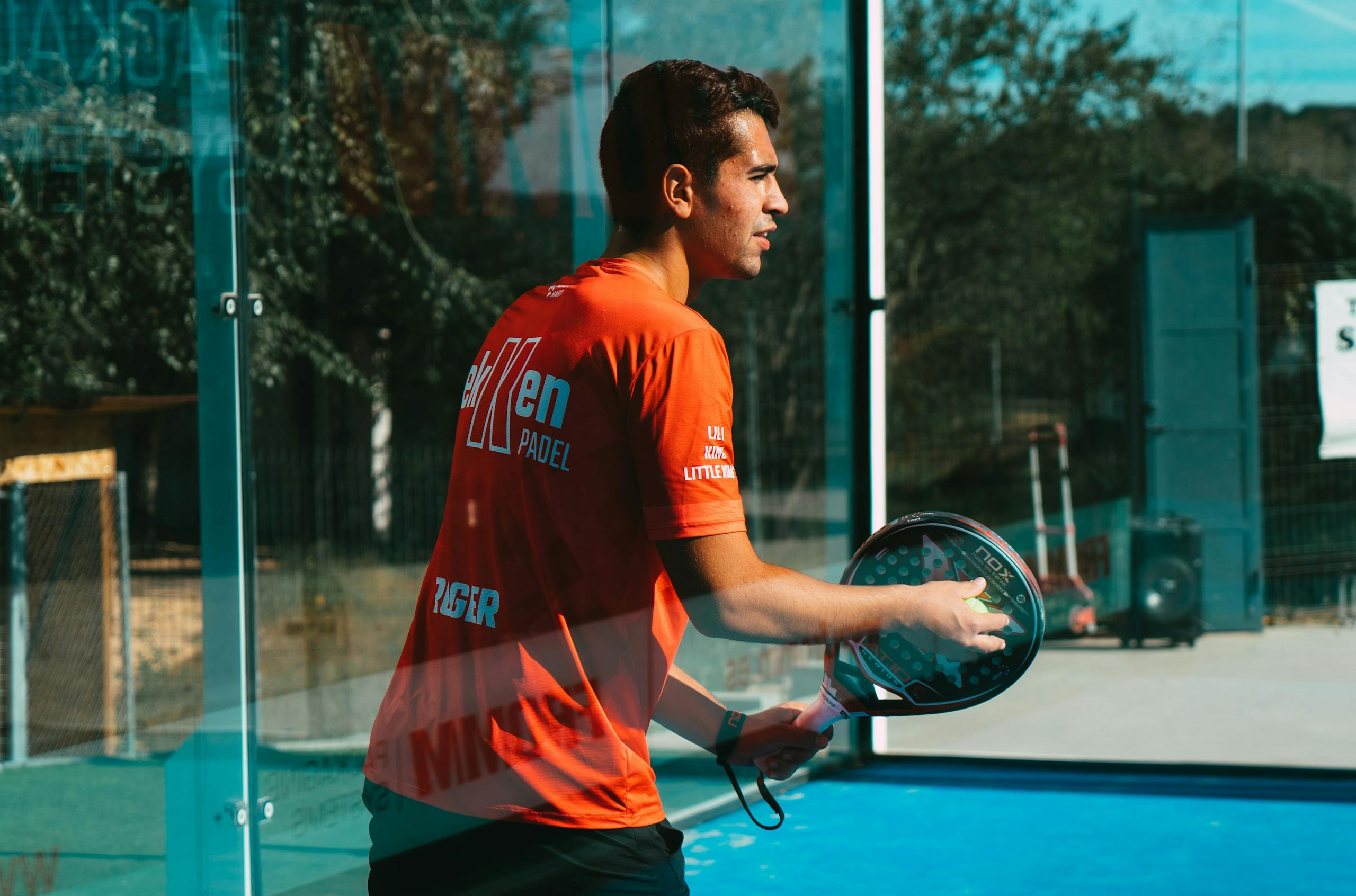 A focused young man practices padel tennis outdoors on a sunny day, showcasing skill and concentration.