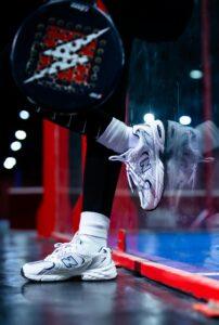 Close-up of person with padel racket and sneakers on a vibrant court.