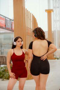 Two women in sporty outfits wearing headphones in a modern urban environment.